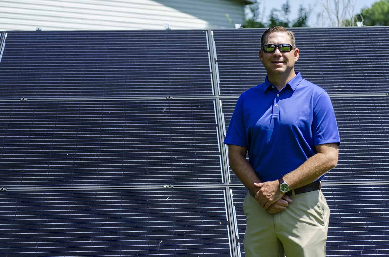 Photo of Brent Clinton stands next to solar panels