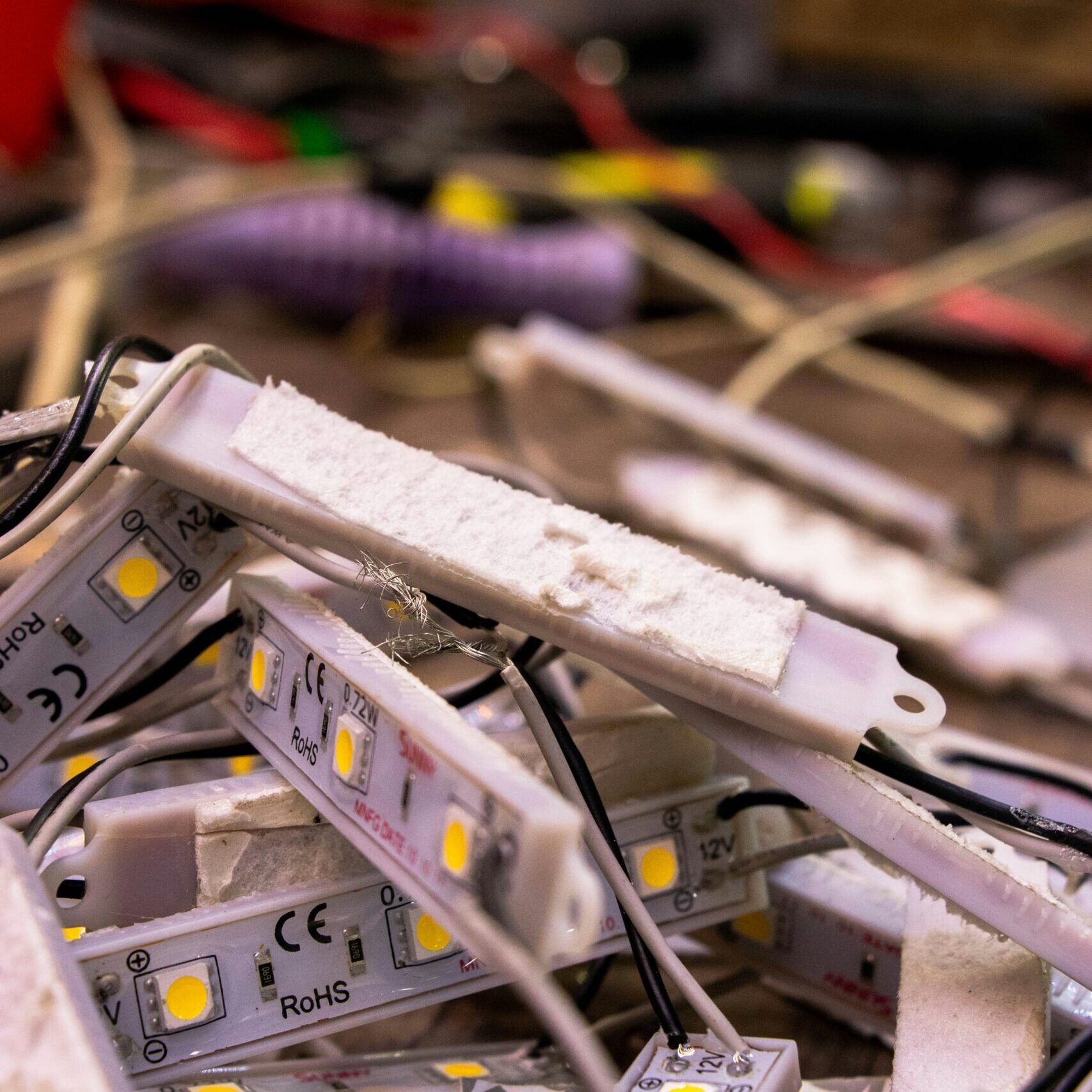 A pile of disconnected LED light strips and wires, amidst a cluttered workspace, suggesting repair or assembly in progress.