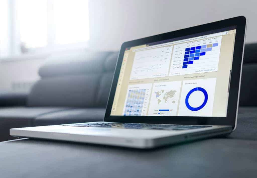 A laptop displays various data visualizations, including charts and graphs, on a sofa in a well-lit room.