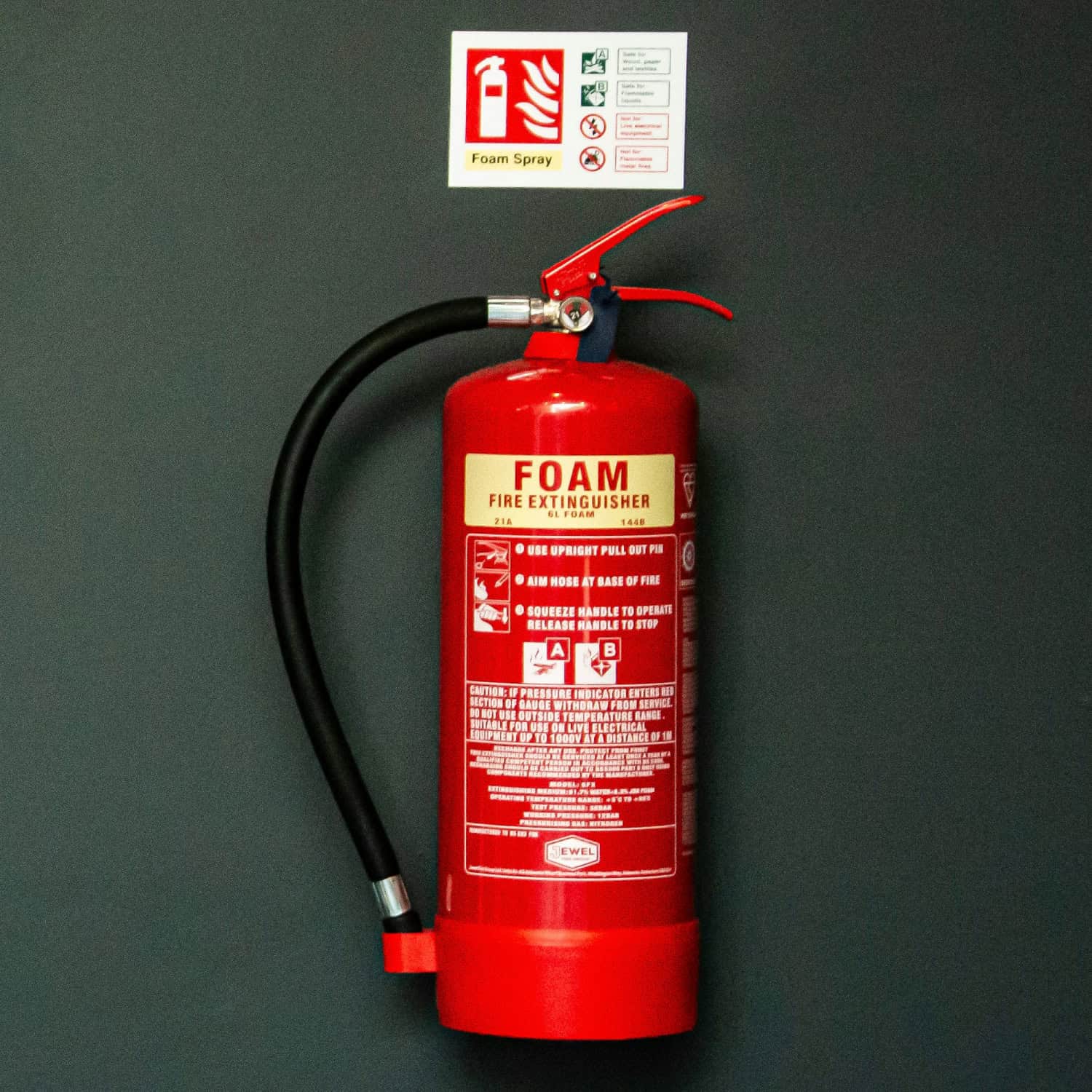 A red foam fire extinguisher hangs on a gray wall with an instructional sign above, showing usage steps and safety icons.