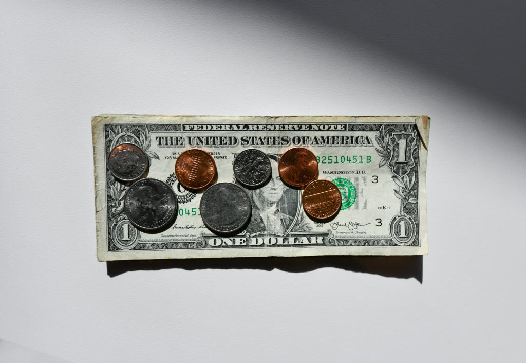 A U.S. one-dollar bill with several coins of varying denominations placed on top, casting shadows on a plain surface.