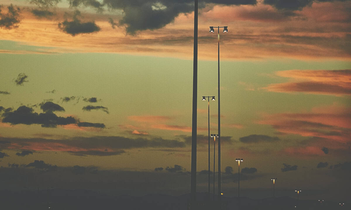 Streetlights illuminated against a colorful sunset sky with scattered clouds, casting a serene urban atmosphere without visible landmarks.