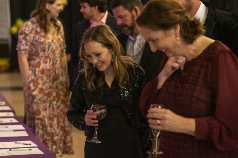 Two women sip wine and peruse the auction items.