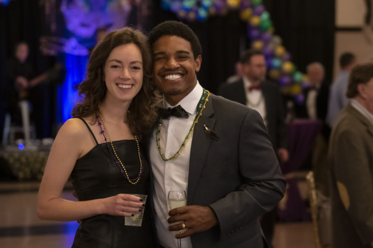 Two attendees smile for the camera and sip champagne.