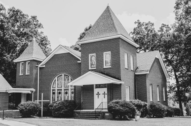 A red brick church with stained glass windows is pictured in black and white.