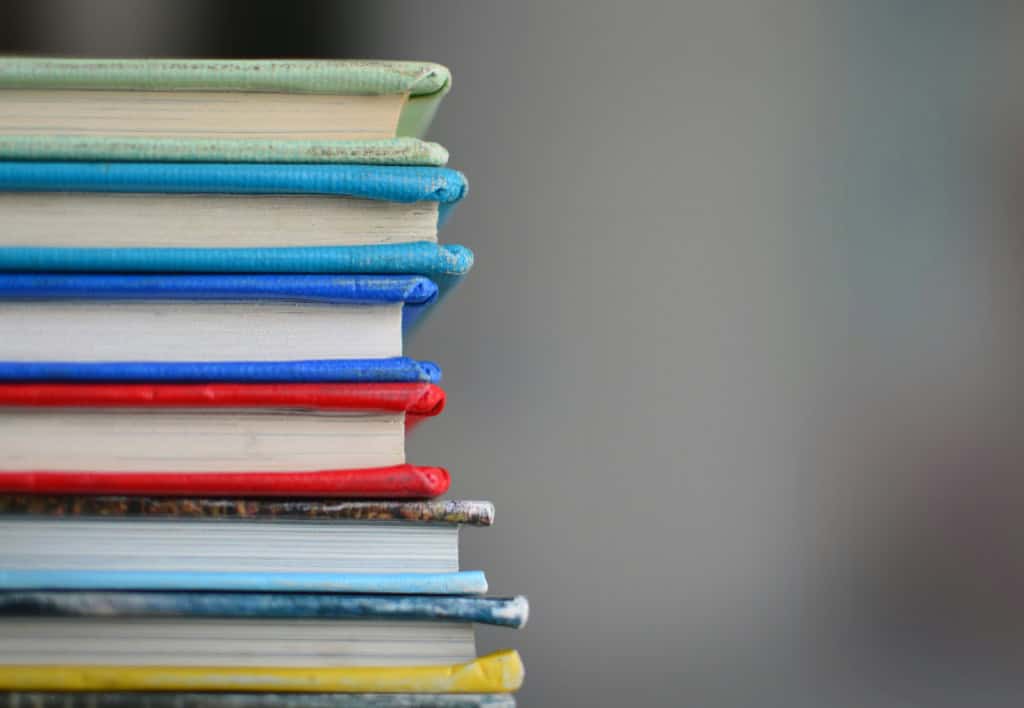 A vertical stack of colorful hardcover books with a blurred gray background, emphasizing reading and education themes.