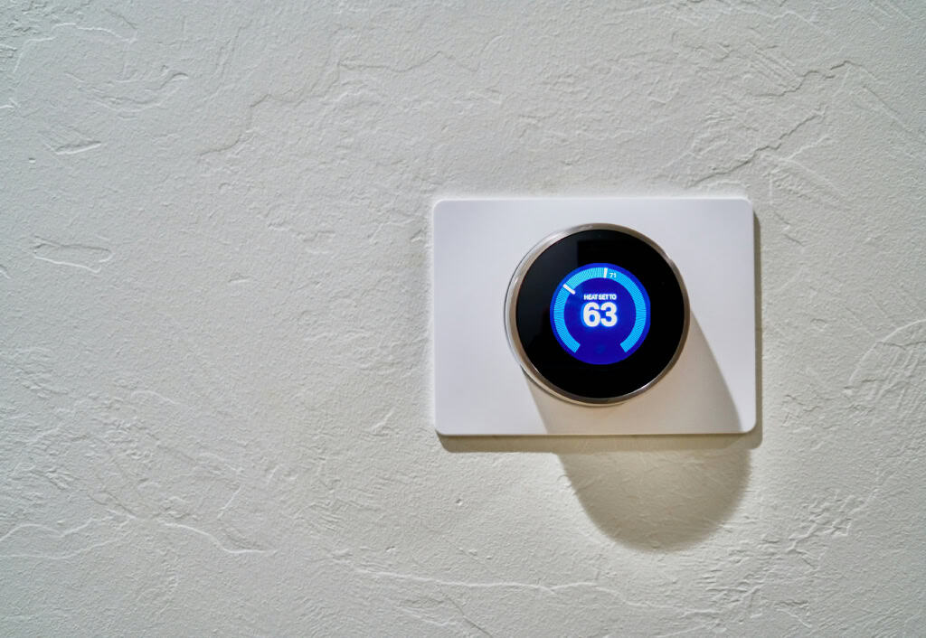 A modern, round digital thermostat mounted on a textured wall, displaying a temperature setting of 63 degrees Fahrenheit.