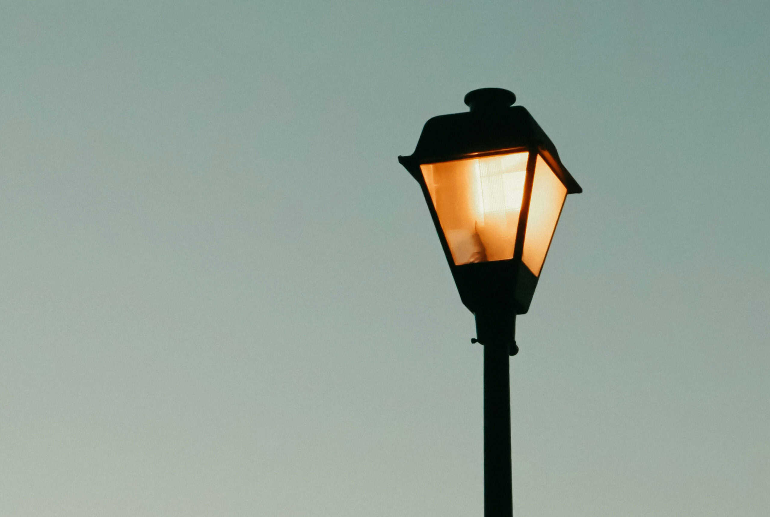 Old-fashioned streetlight against a clear, dusk sky, softly illuminated, evoking a nostalgic atmosphere.