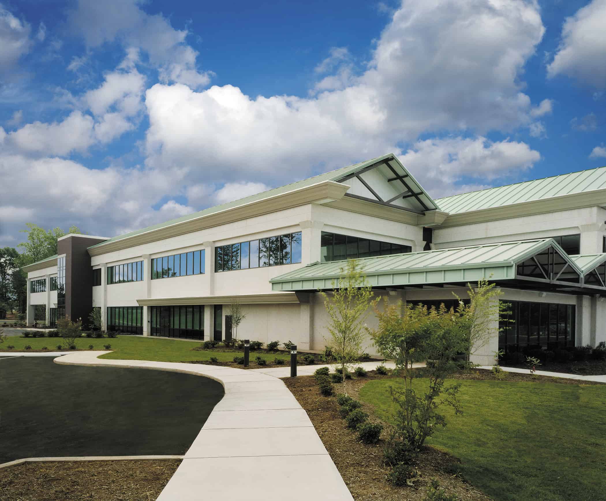 Modern two-story building with large windows and green roof, surrounded by a well-maintained lawn and pathway, under a partly cloudy sky.